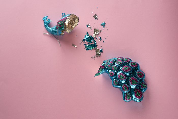 Broken Christmas Toy. Crashed bauble. Damages Gorgeous glass peacock on pink background.