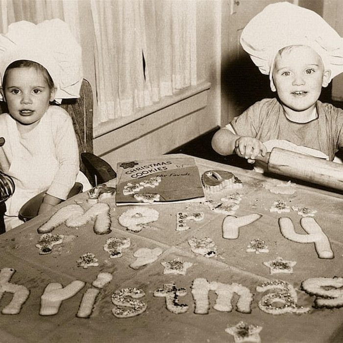 Black and white photo of two kids spelling out "Merry Christmas" with cookies