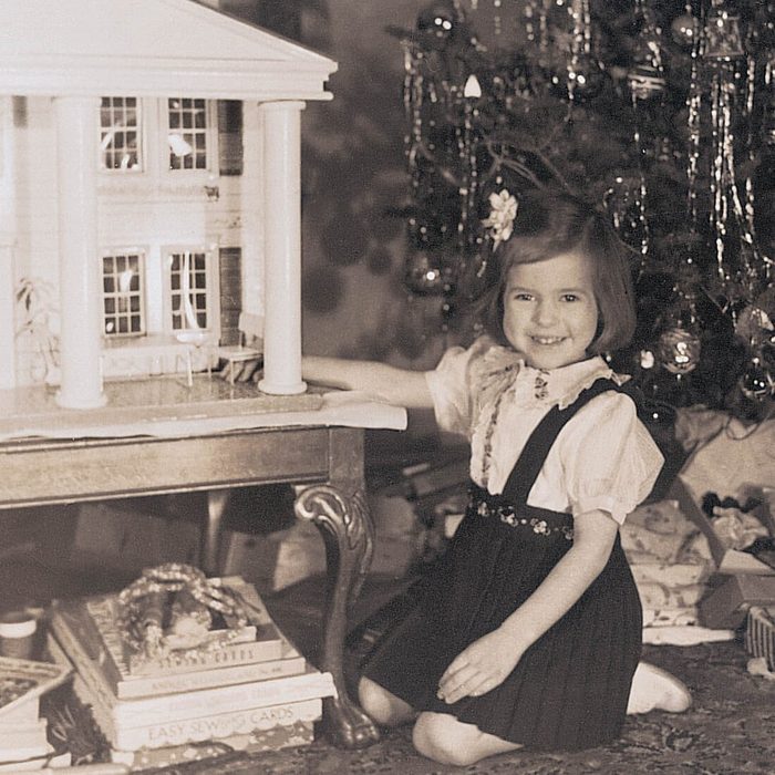 Black and white photo of a young girl beside a dollhouse