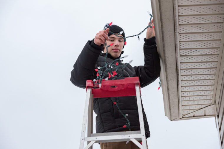 Man hanging Christmas lights during winter from a ladder