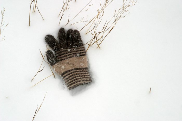 The lost children's woolen glove lies on the white snow. Winter background