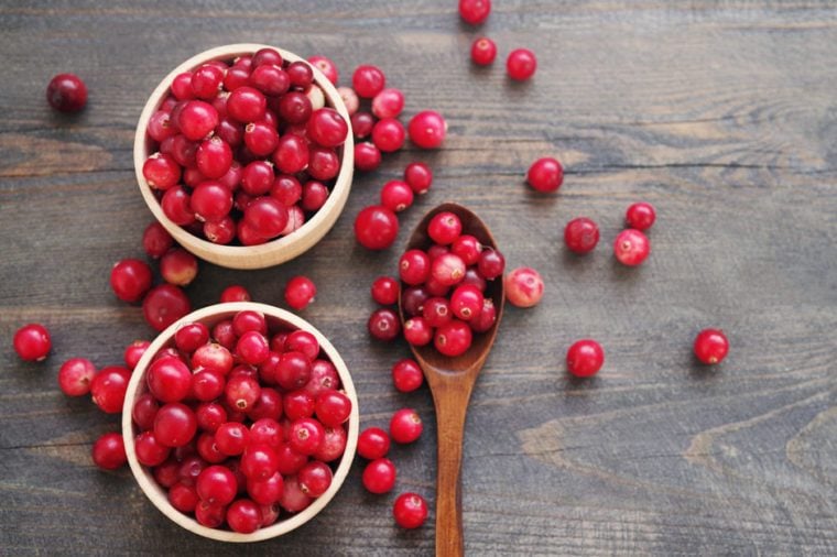 Fresh juicy cranberry in wooden round bowls with a wooden spoon on a table, close up