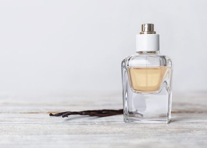 Perfume bottle and vanilla pods on wooden table against light background