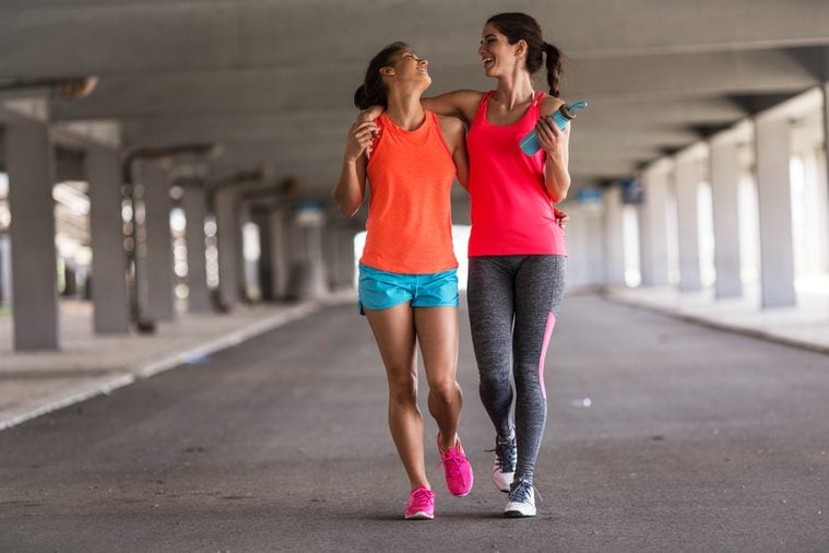 Couple of female friends jogging on the city street under the city road overpass.They relaxing after jogging and making fun.Embracing each other.