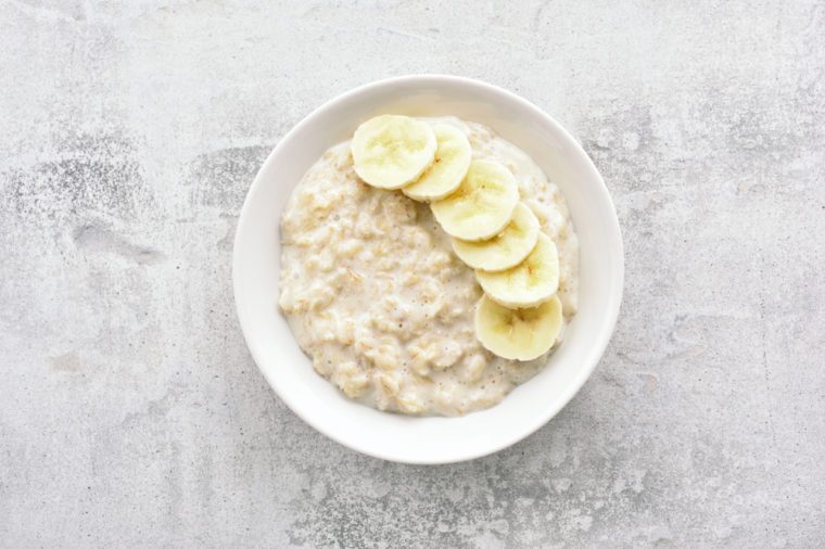 Oats porridge with banana slices in bowl over stone background. Diet healthy nutrition food concept. Top view, flat lay