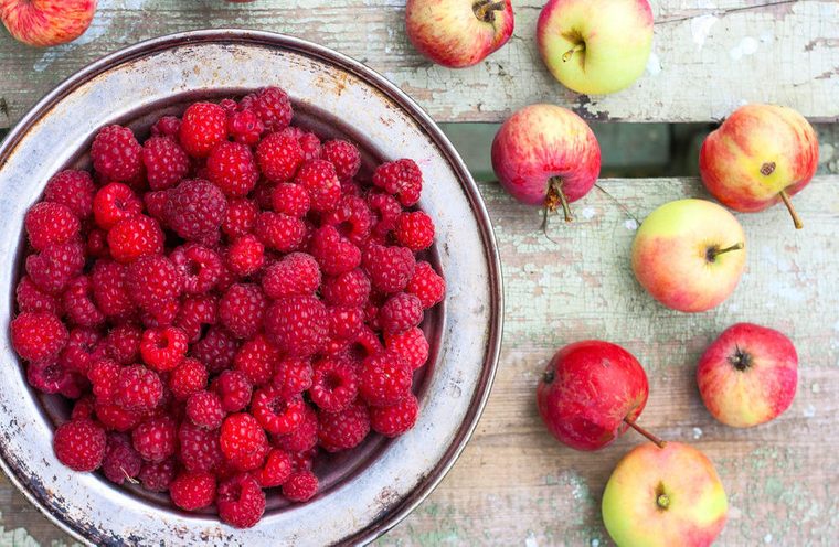 fresh harvested raspberries in a metal bowl on a wooden table. Around lie fresh apples