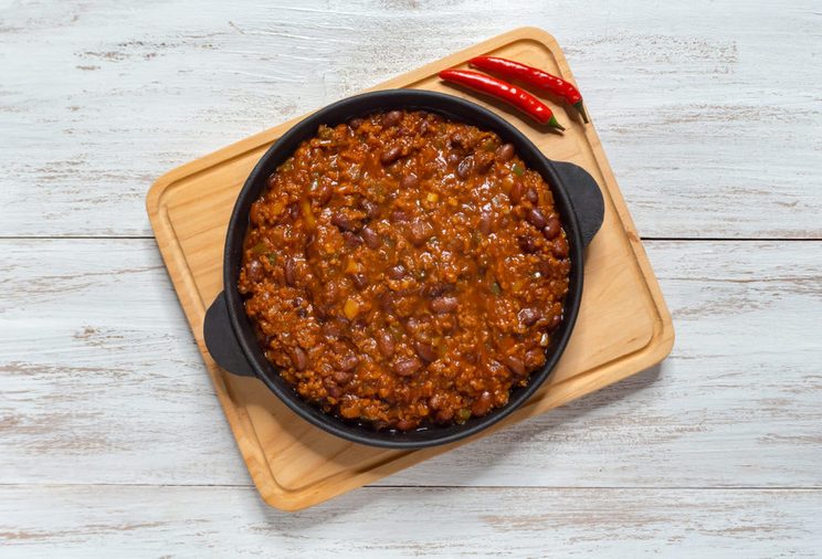 Mexican chili. Chili con carne in frying pan on white wooden background.