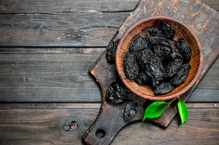 Prunes with green leaves in the bowl. On a wooden background.