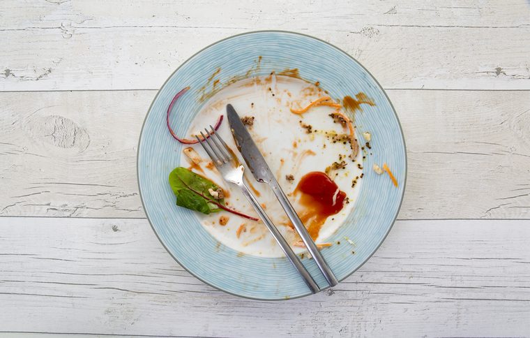 Overhead shot of an empty plate with leftovers from a meal on a white wooden backround