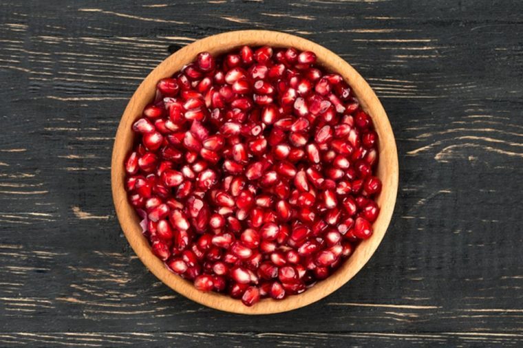 Fresh pomegranate seeds in bowl on a blank wooden background