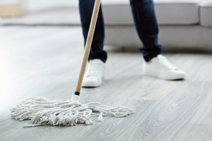 Young man with mop cleaning floor at home, closeup