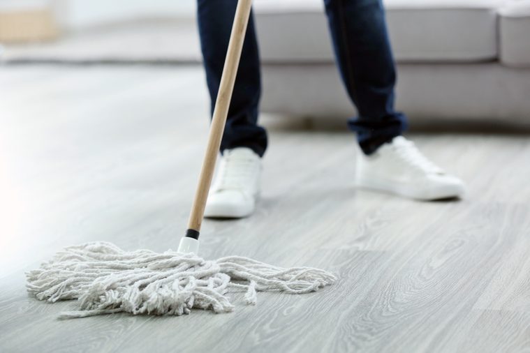 Young man with mop cleaning floor at home, closeup