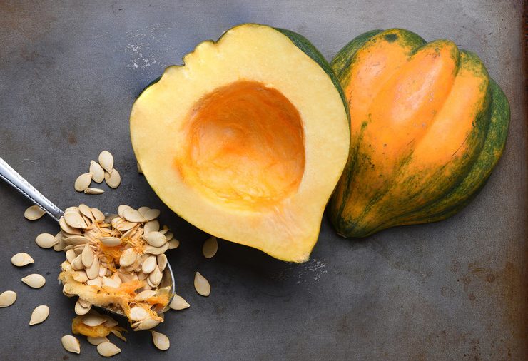 High angle view of an Acorn Squash cut in half on a metal baking sheet with a spoon and seeds scooped out.