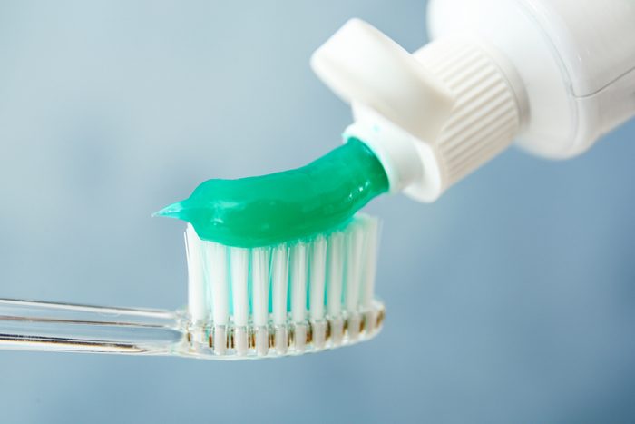 Squeezing toothpaste on brush against color background, closeup