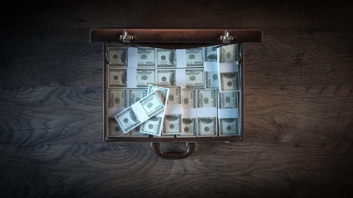 Elegant open briefcase filled with dollar packs on a wooden desktop in the dark, top view