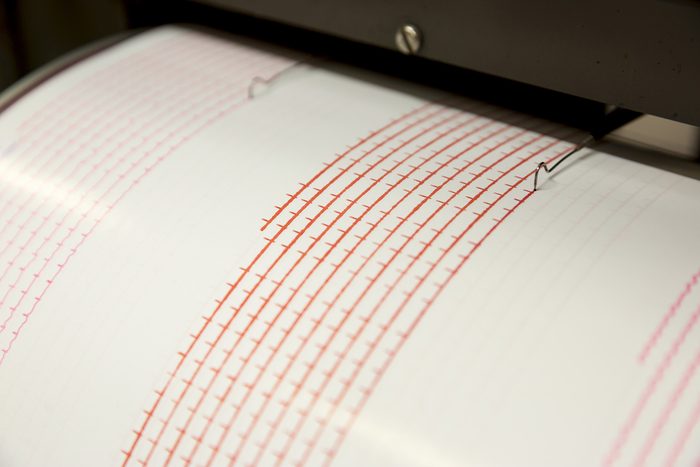 Seismograph records an earthquake on the sheet of measuring paper. Seismological device for measuring earthquakes. Seismograph machine needle drawing a red line on graph paper measuring activity.