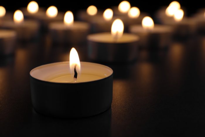 Burning candle on table in darkness, closeup with space for text. Funeral symbol