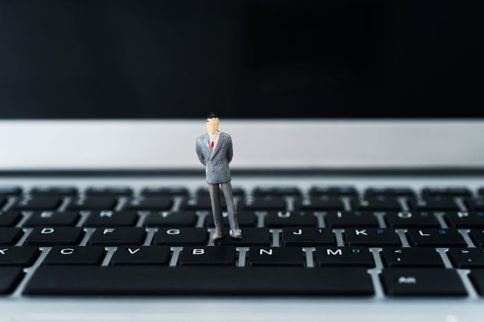 Miniature businessman standing on laptop keyboard.