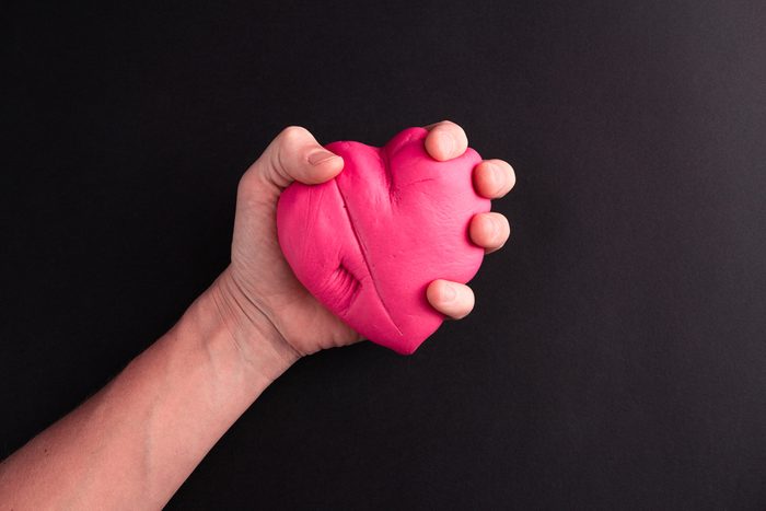 Mens hand squeezing pink heart on a black background