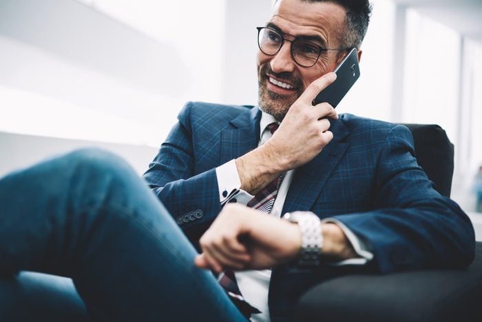 Successful entrepreneur middle aged laughing during phone conversation on smartphone sitting in office.Prosperous businessman in formal wear calling on cellphone.Cheerful proud ceo talking on cellular