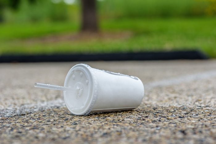paper soft drink cup with plastic lid and straw thrown on the side of the road - littering concept
