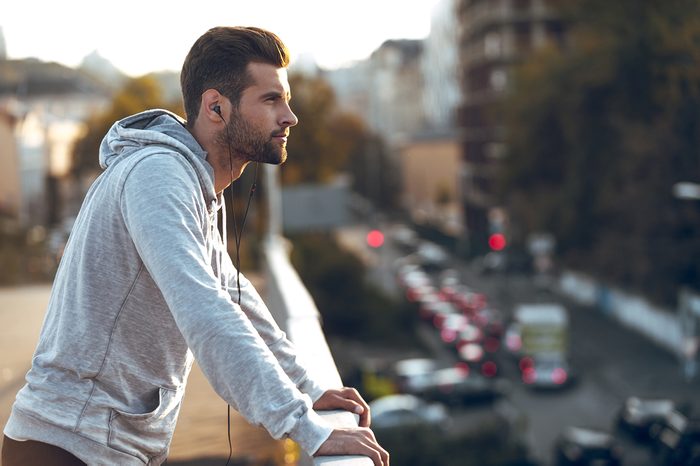 In love with his city. Side view of pensive young man in headphones looking away while standing on the bridge