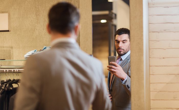 sale, shopping, fashion, style and people concept - young man in suit with smartphone taking mirror selfie at clothing store