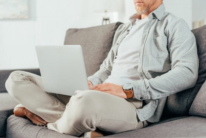 cropped shot of man sitting on couch and using laptop