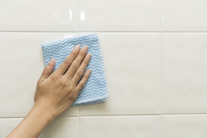 Cleaning tile wall by woman hand