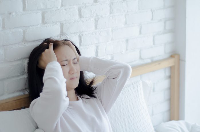 Asian women are headache severely.Lady wake up in the morning with migraine. Insomnia results in headaches when awakened.Young girl sitting on a stressed bed. In her bedroom.She was sick.