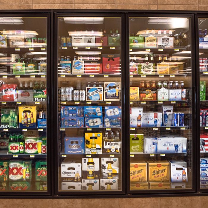 Various bottles of craft, microbrew, IPA, domestic and imported beers from around the world on shelf display in supermarket cooler.