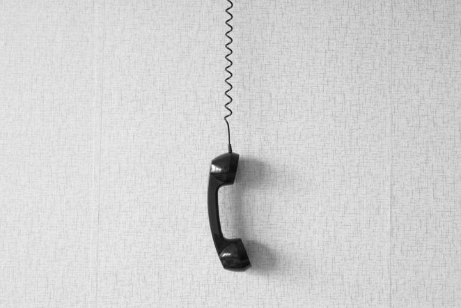 black old handset with a wire hang against wallpaper texture. black plastic telephone hanging by the cord.Retro Phone Cord - Vintage Telephone Handset Receiver hanging by the Cord down