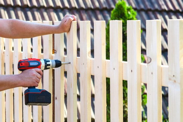 building a wooden fence with a drill and screw. Close up of his hand and the tool in a DIY concept.