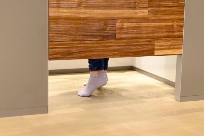 Woman standing on tip toe in a changing room at a store as she tries on clothes, view of her feet under the wooden door