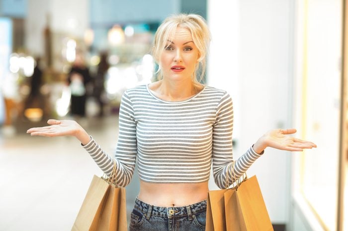 Spent all the money. Beautiful mature woman looking confused spreading her arms at the shopping mall after spending all her money broke poor no money helpless confused lost perplexed shopaholic