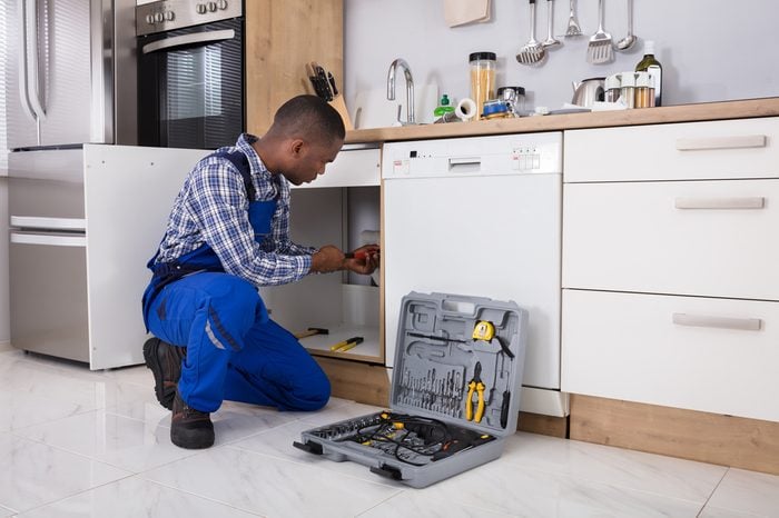 African Male Plumber Fixing Sink Pipe In Kitchen