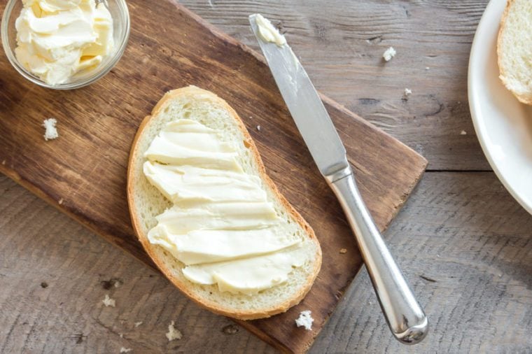 Butter and bread for breakfast, with knife over rustic wooden background, top view