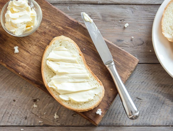 Butter and bread for breakfast, with knife over rustic wooden background, top view