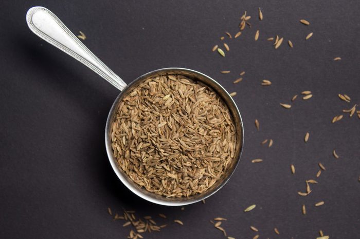 Organic caraway or cumin seeds in a metallic bowl on a dark floor