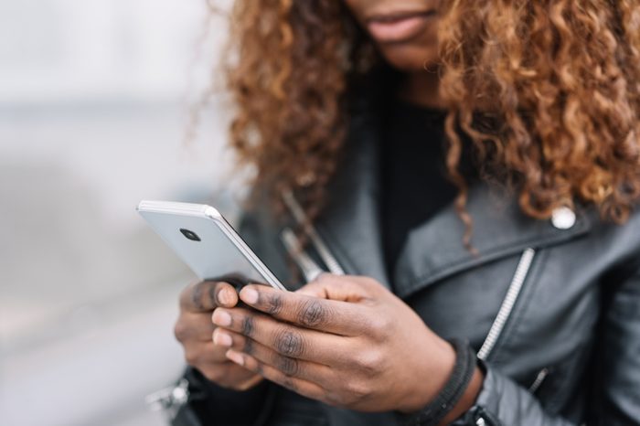 Close up view of curly-haired black woman holding mobile phone