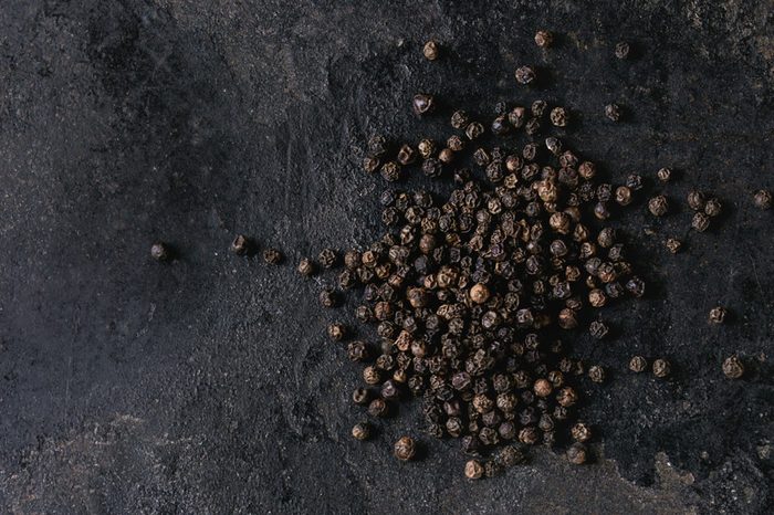 Heap of black pepper peppercorns over old black iron texture background. Top view, copy space. Square image