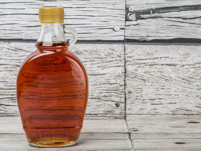 Maple syrup in glass bottle over wooden background