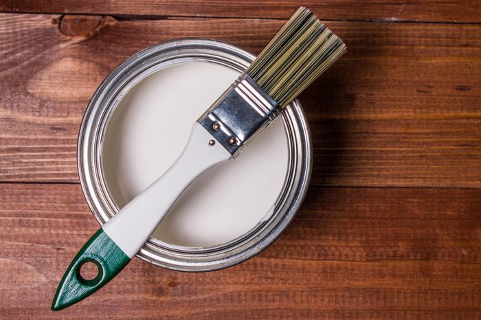 A set of white paint brushes, a metal can with white paint on a wooden table