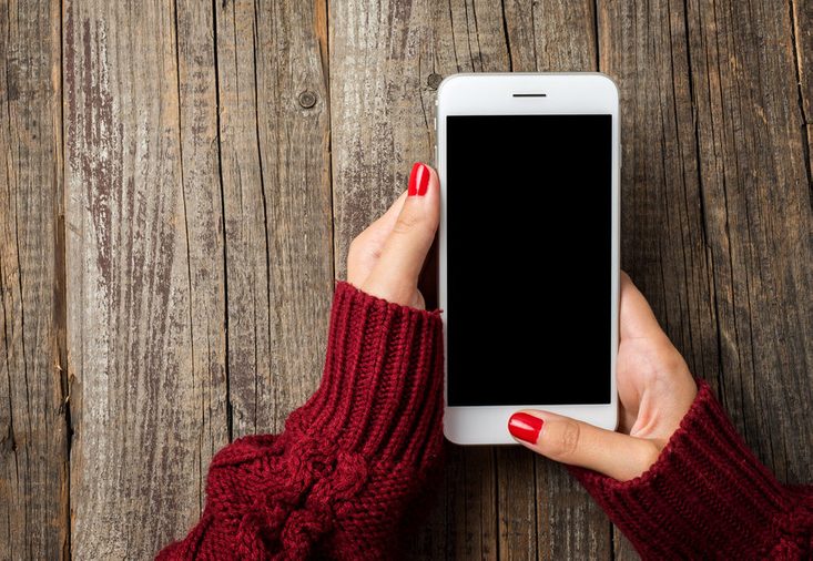Female hands in warm sweater holding white smart phone