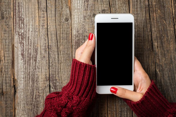Female hands in warm sweater holding white smart phone