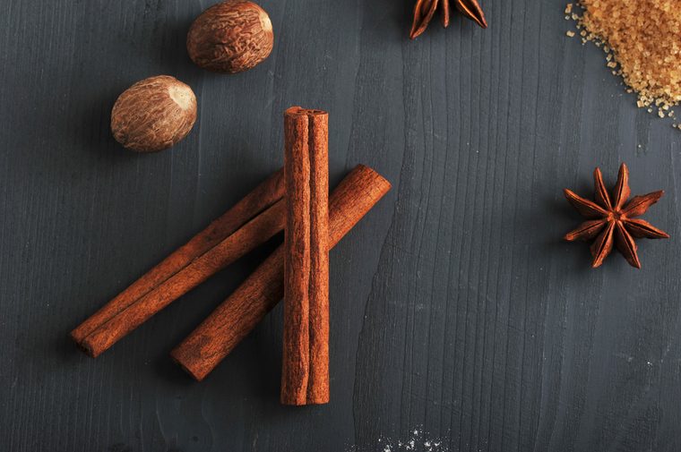 In the frame, cinnamon sticks, nutmeg, cane sugar and anise. Spices for cooking homemade cookies. Dark wooden surface. View from above. Close-up.