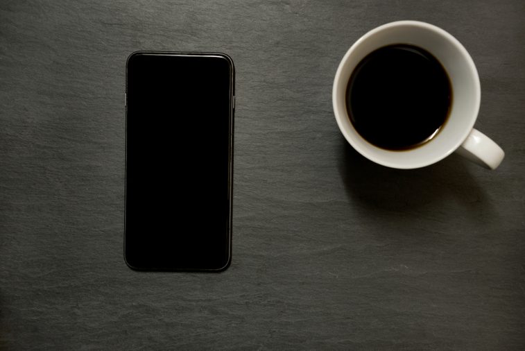Mobile phone/ smart phone and cup of coffee - from above on dark slate table top background, with copy space