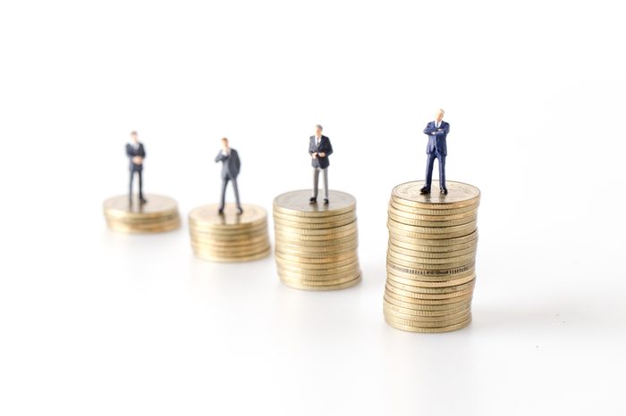 miniature model group of businesspeople standing together with coin isolated on white background.