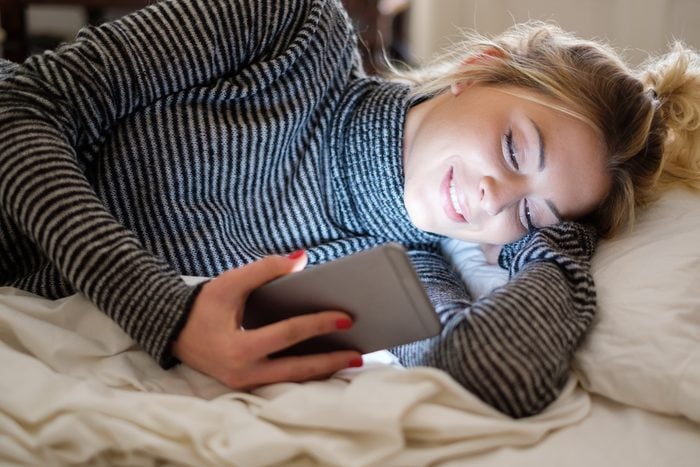 Teenage girl relaxing in bedroom reading phone news feed