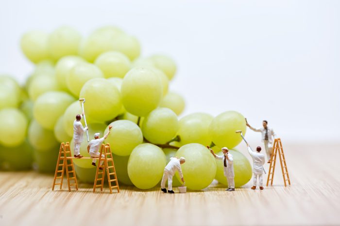Group of miniature people washing bunch of white grape.